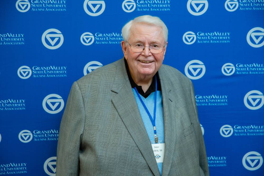 An alumnus poses for a photo in front of the Grand Valley's backdrop at the Reunion Dinner.